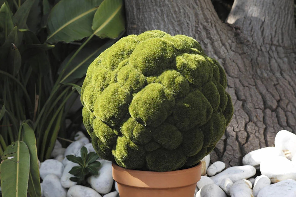 Bola de musgo artificial en un jardín, junto a un tronco y piedras blancas